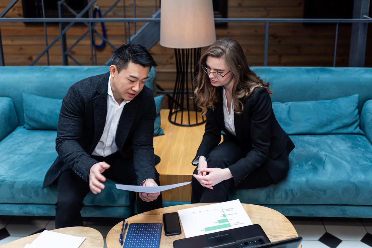 Two people sitting on a couch looking at papers.