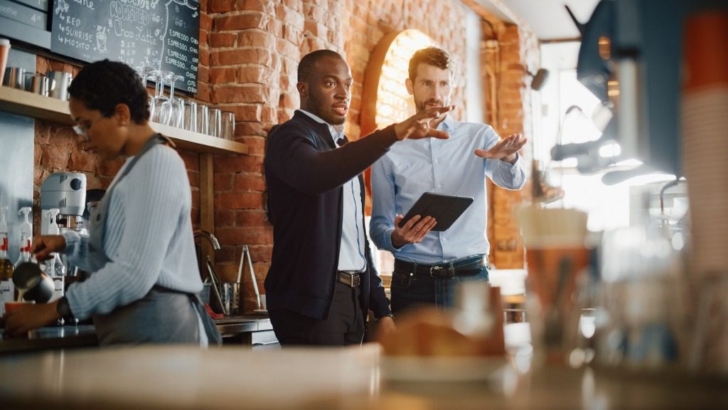 Two men are standing in a bar with one man holding an ipad.